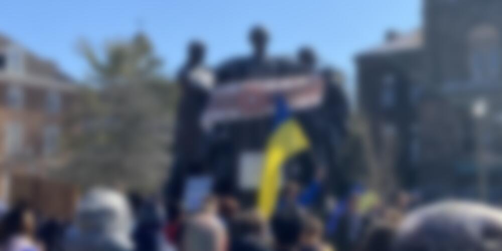 Image of the Alma Mater statue holding a Ukrainian banner with a crowd of people