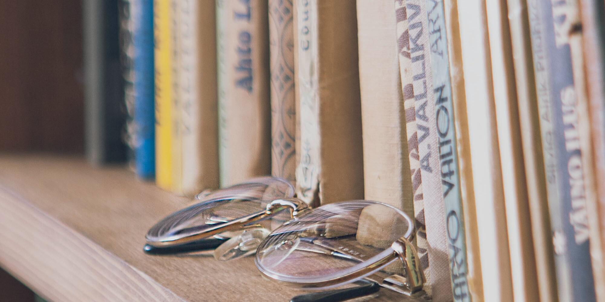 books on a shelf with folded glasses sitting in front of them