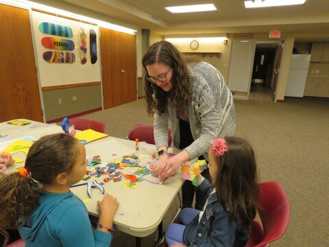 a woman helping two children with an educational craft